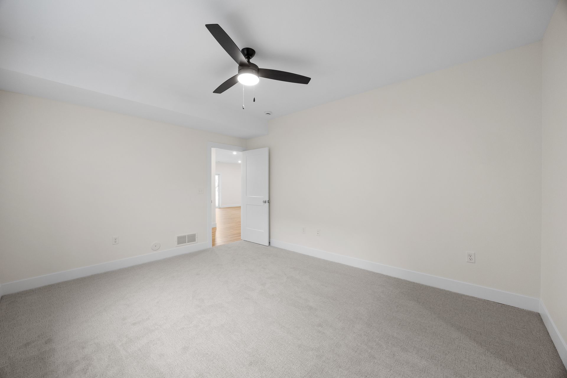 An empty bedroom with a ceiling fan and a door.