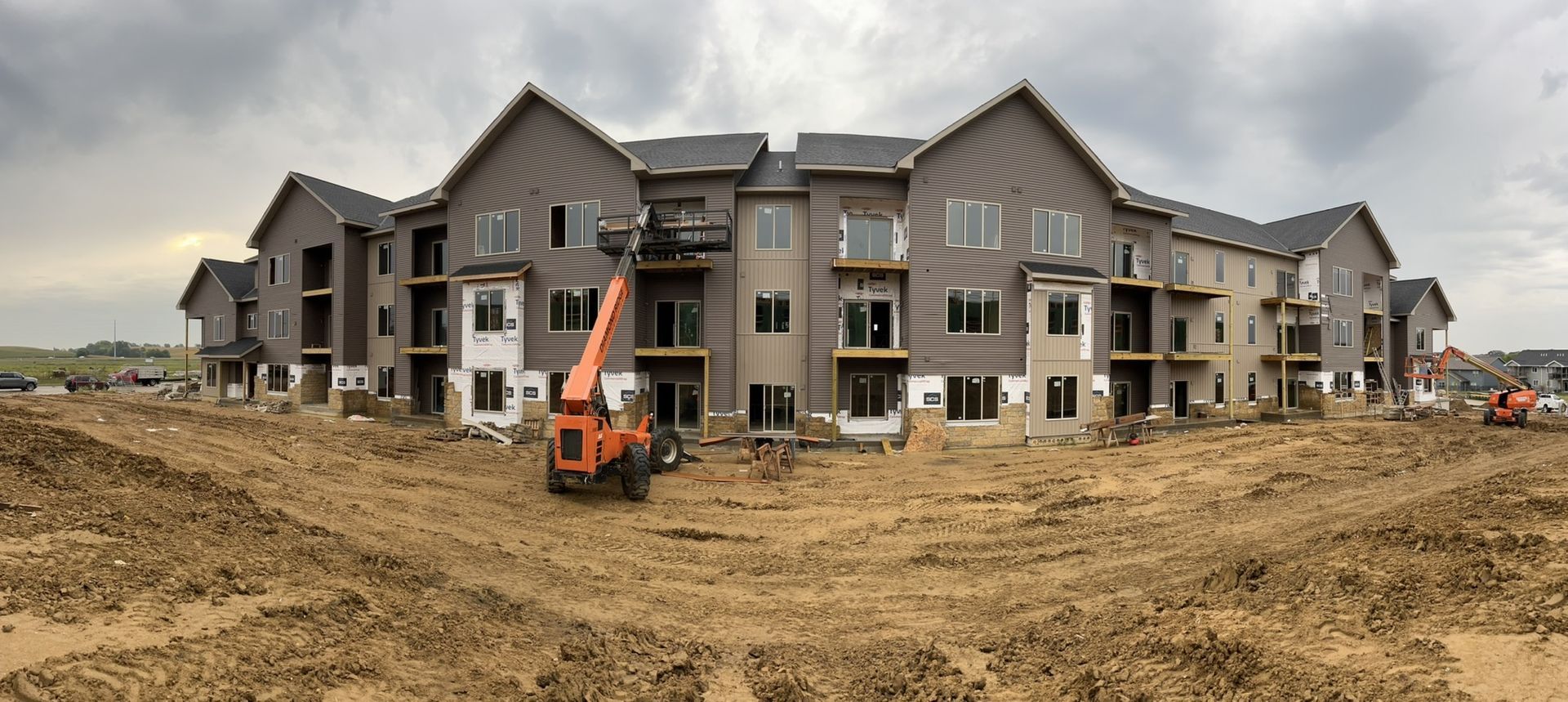 A large apartment building is being built in a dirt field.