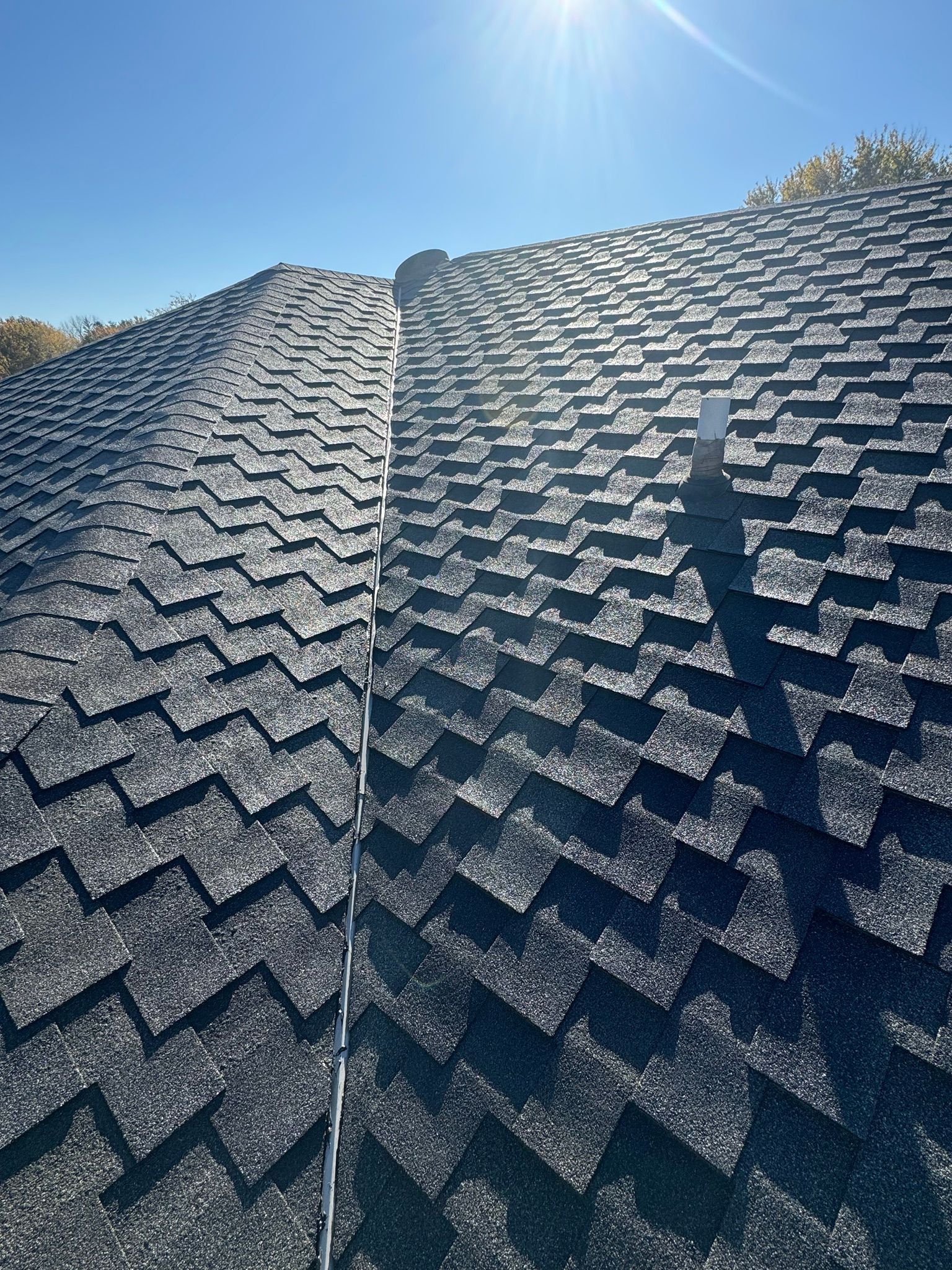 A close up of a roof with shingles and a blue sky in the background.