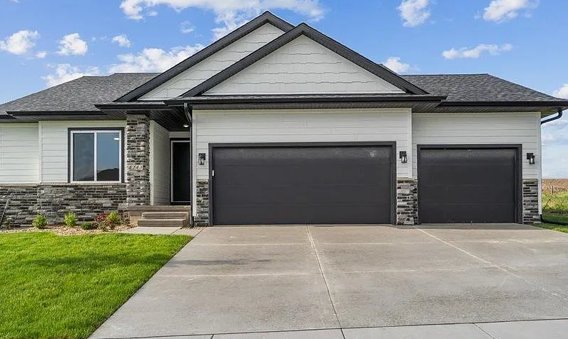 A large white house with two black garage doors and a concrete driveway.