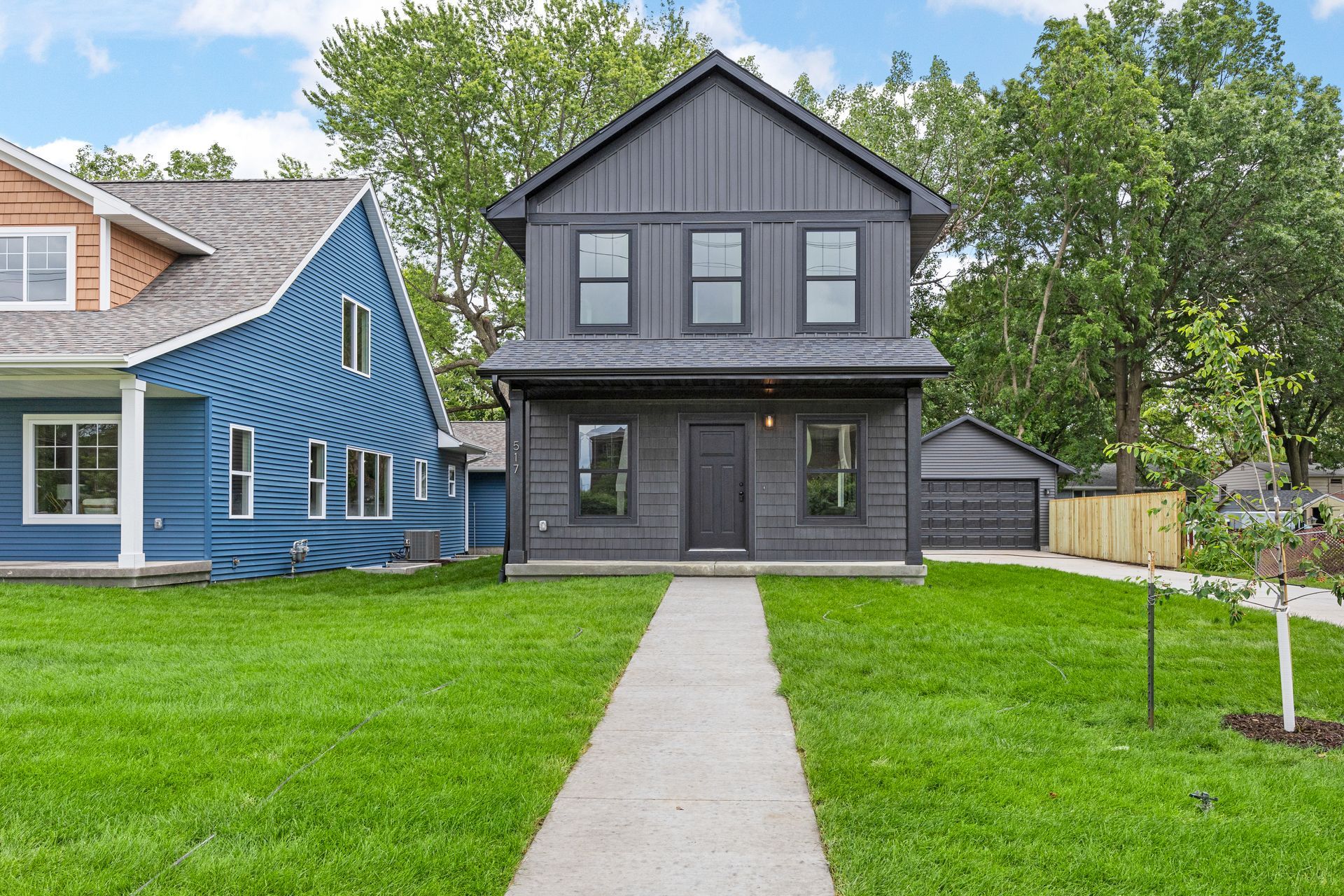 A black house with a blue house in the background is sitting on top of a lush green lawn.