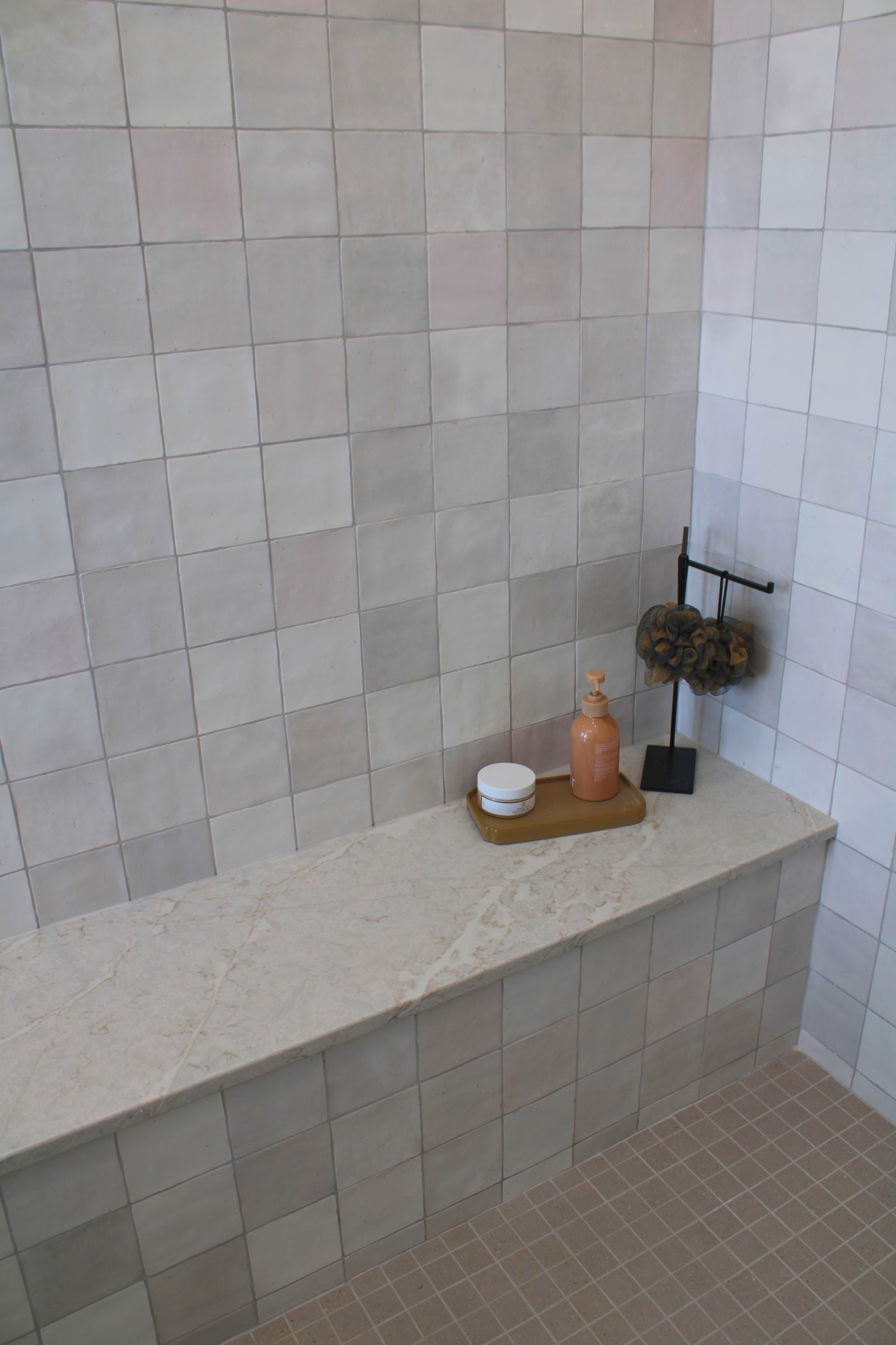 There is a bench in the shower with a vase on it.