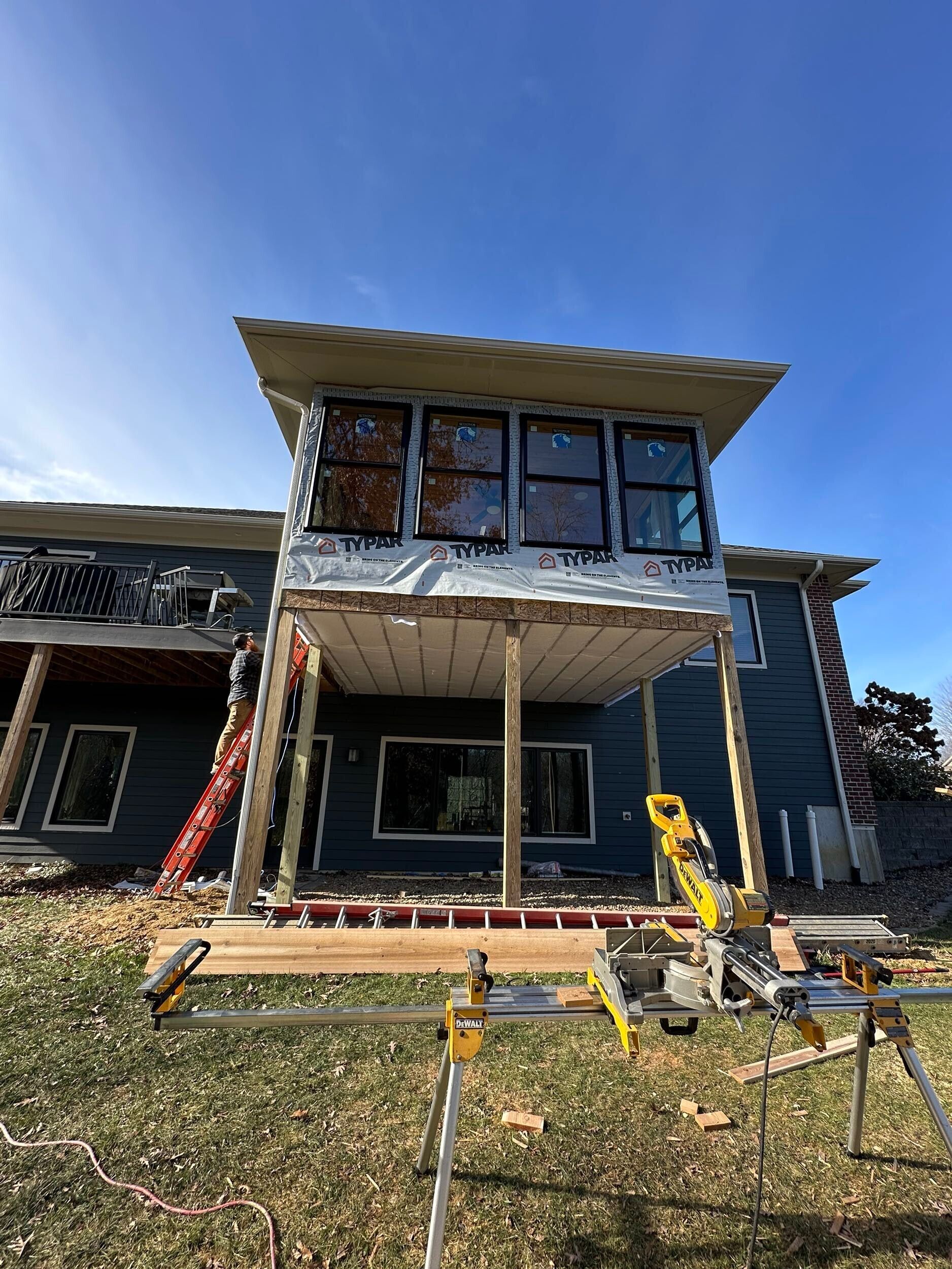 A house is being built with a lot of windows and a table saw in front of it.