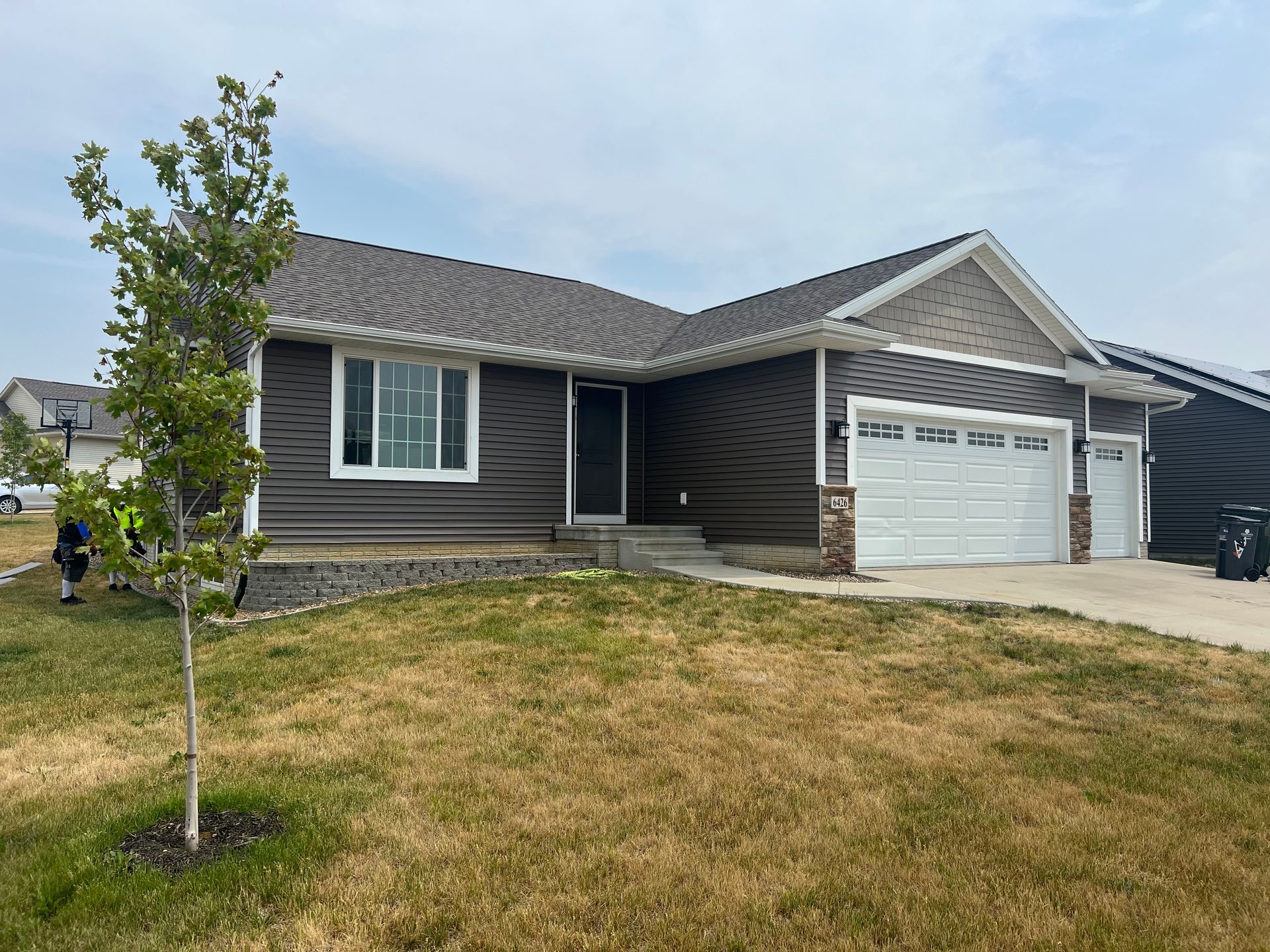 A brown house with a white garage door and a tree in front of it.