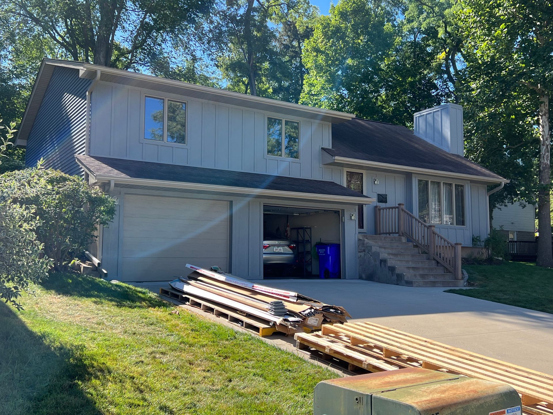 A white house with a garage and a stack of wood in front of it.