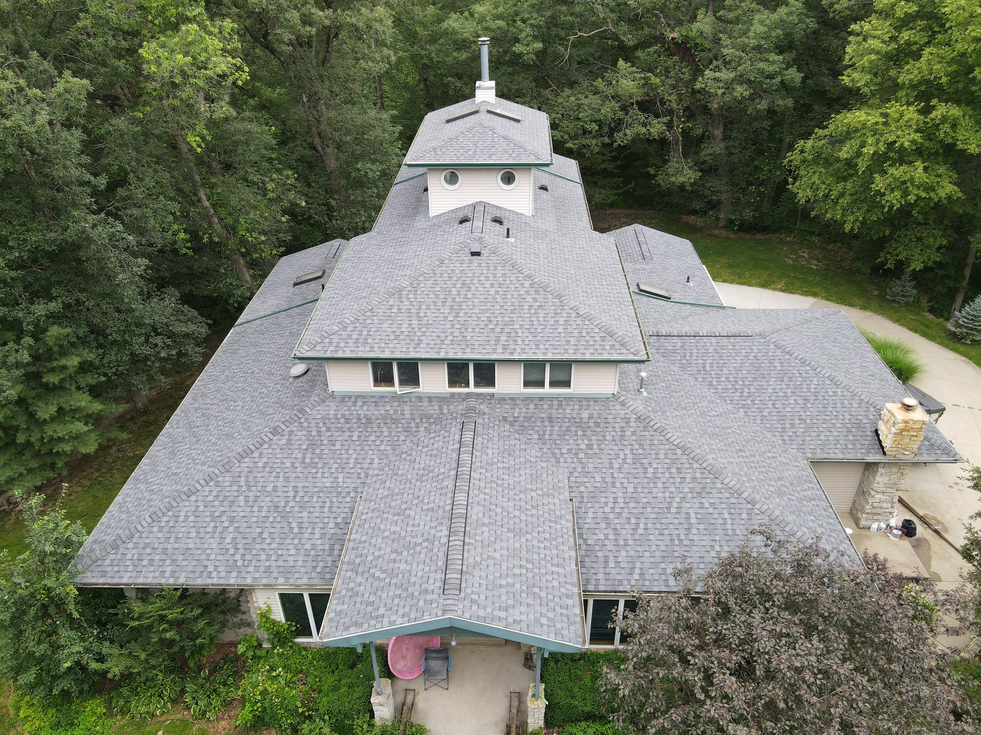 An aerial view of a large house with a gray roof surrounded by trees.