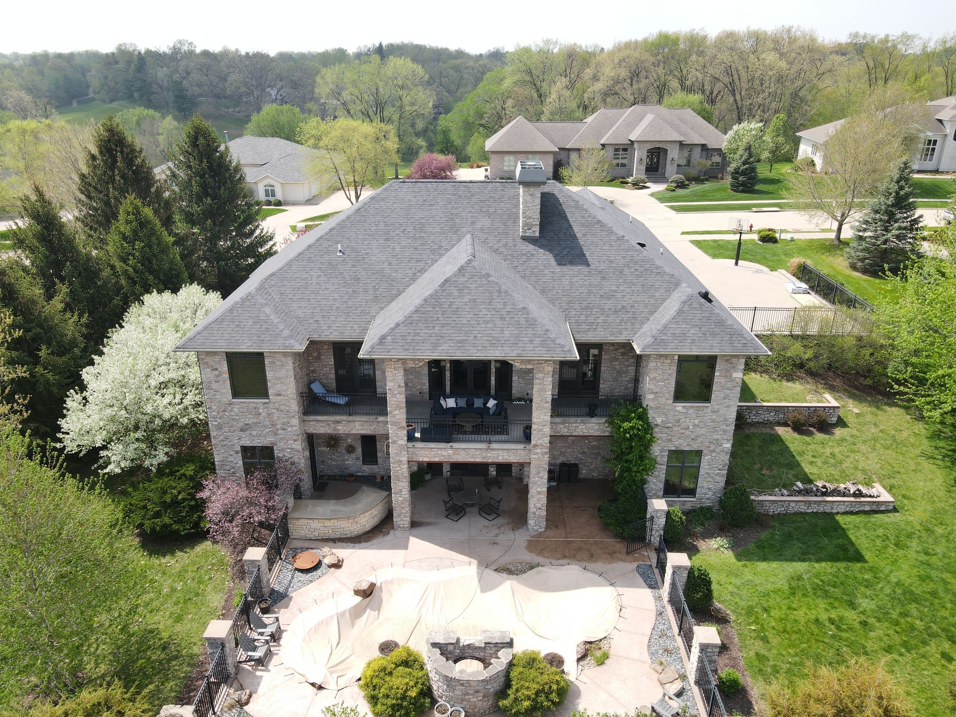 An aerial view of a large house with a gray roof surrounded by trees.