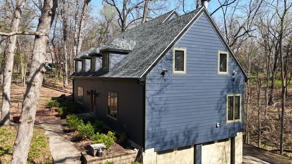 An aerial view of a blue house in the middle of a forest.