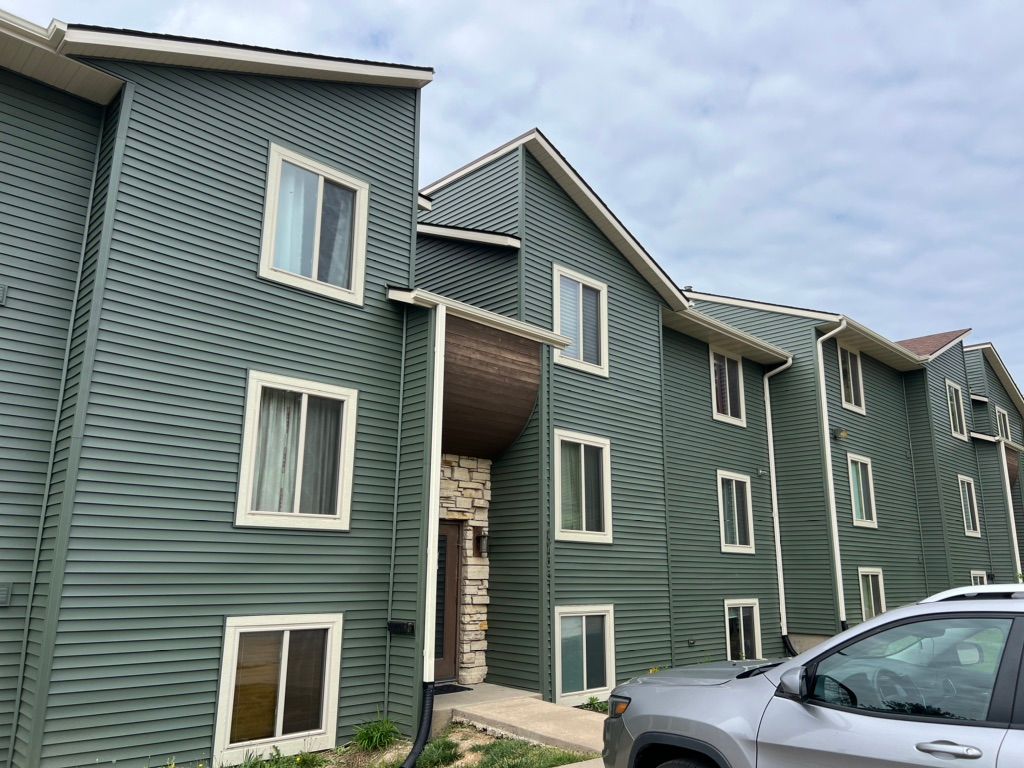 A car is parked in front of a green apartment building.