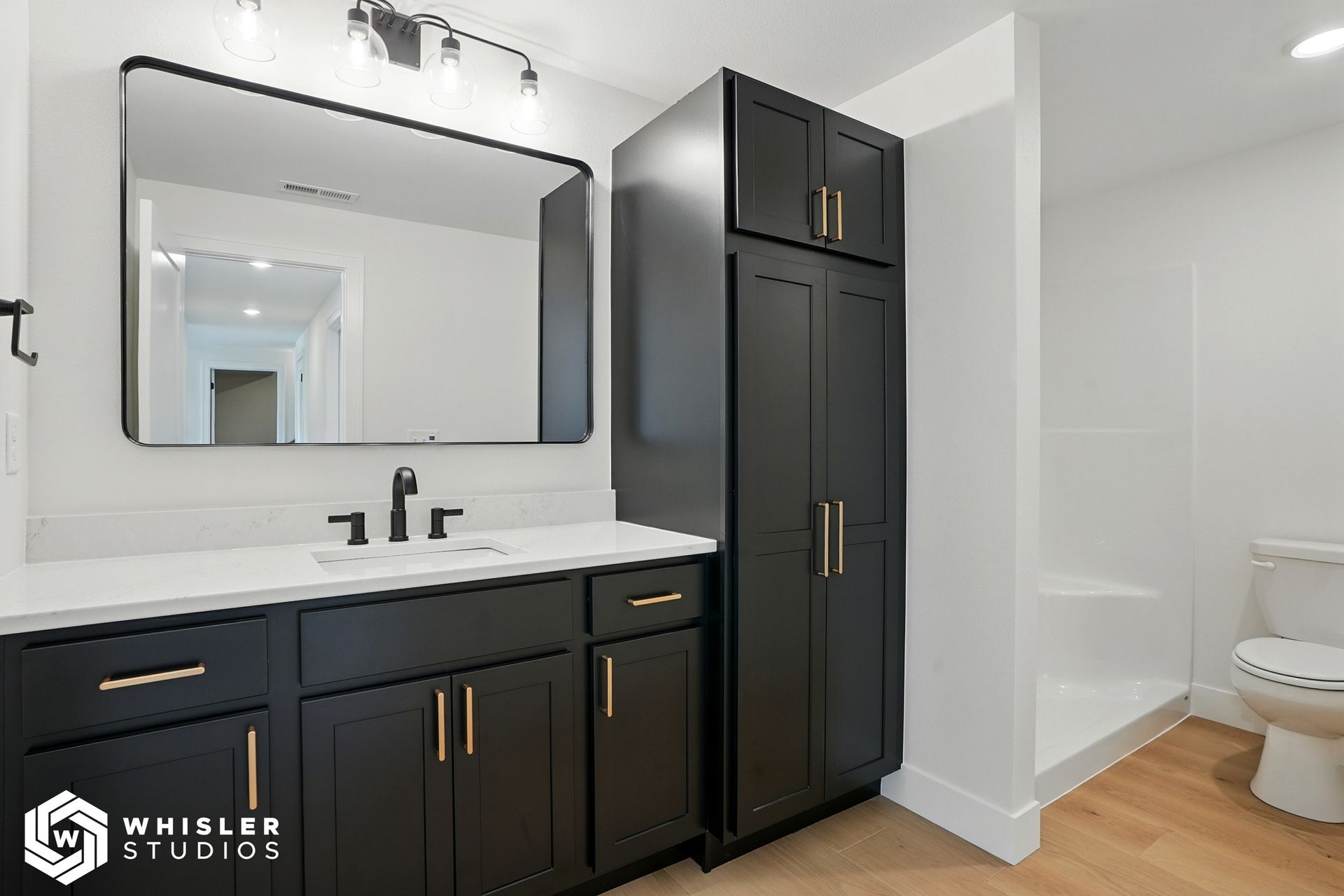 A bathroom with black cabinets, a toilet, and a large mirror.