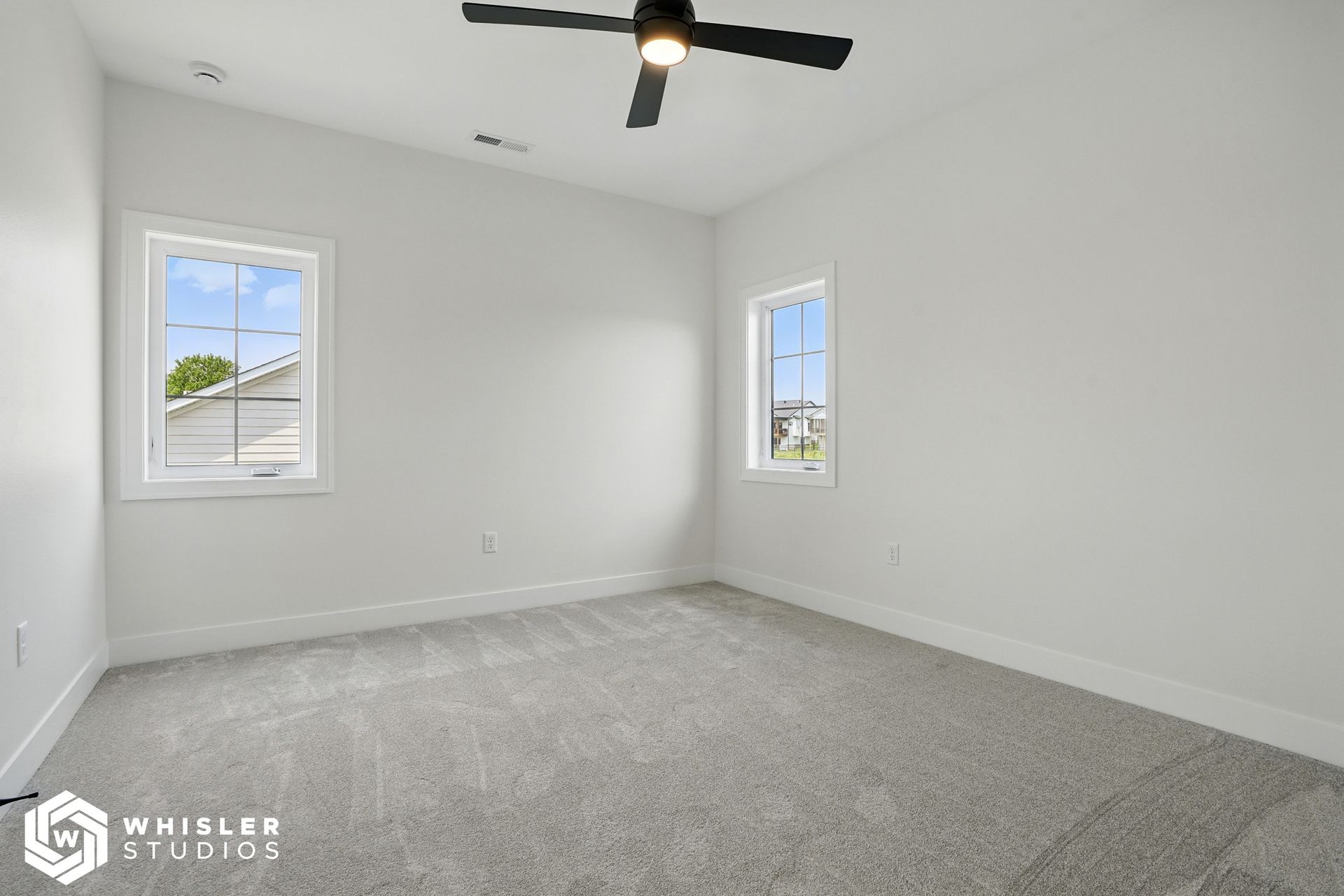 An empty bedroom with a ceiling fan and two windows.