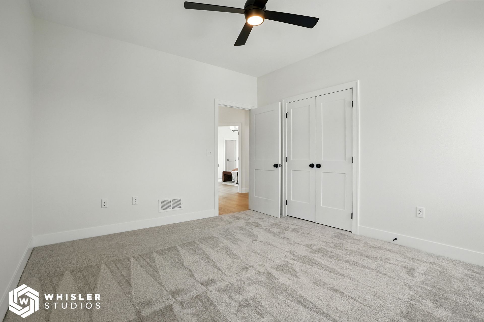 An empty bedroom with a ceiling fan and a gray carpet.