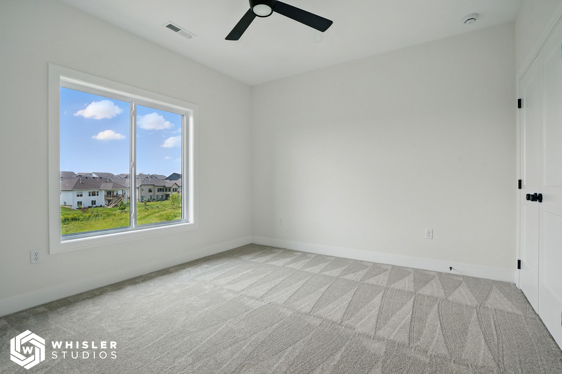 An empty bedroom with a ceiling fan and a large window.