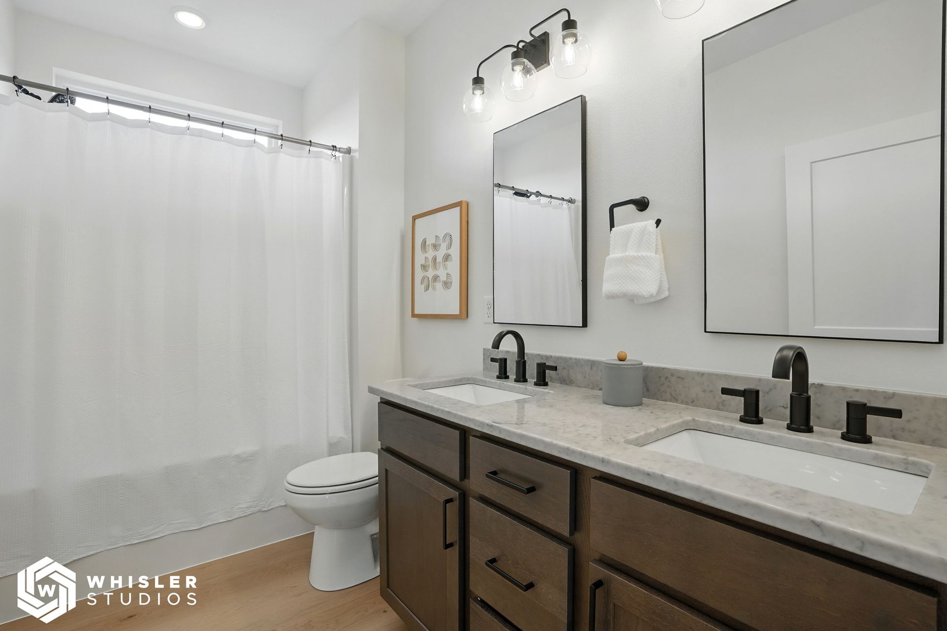 A bathroom with two sinks, a toilet, and two mirrors.