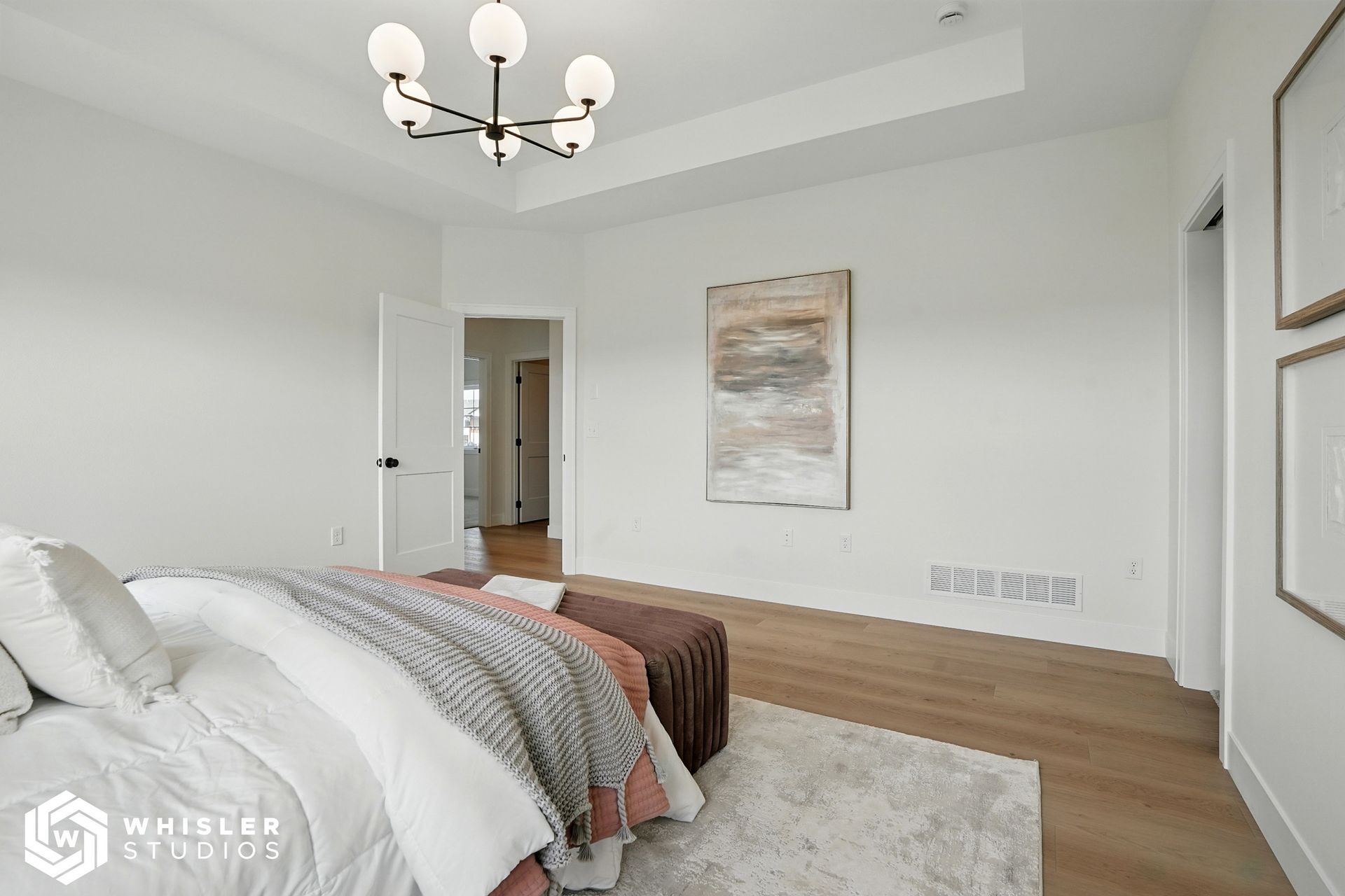 A bedroom with a bed, ottoman, and chandelier.