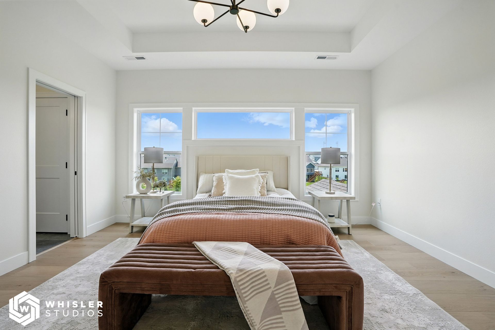 A bedroom with a bed, bench, and two windows.