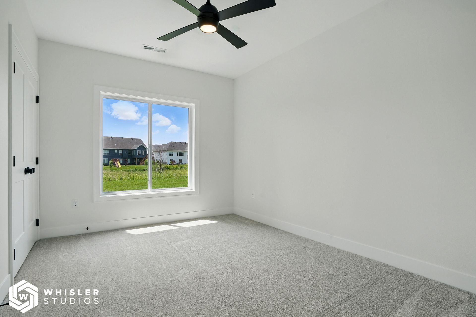 An empty bedroom with a ceiling fan and a large window.