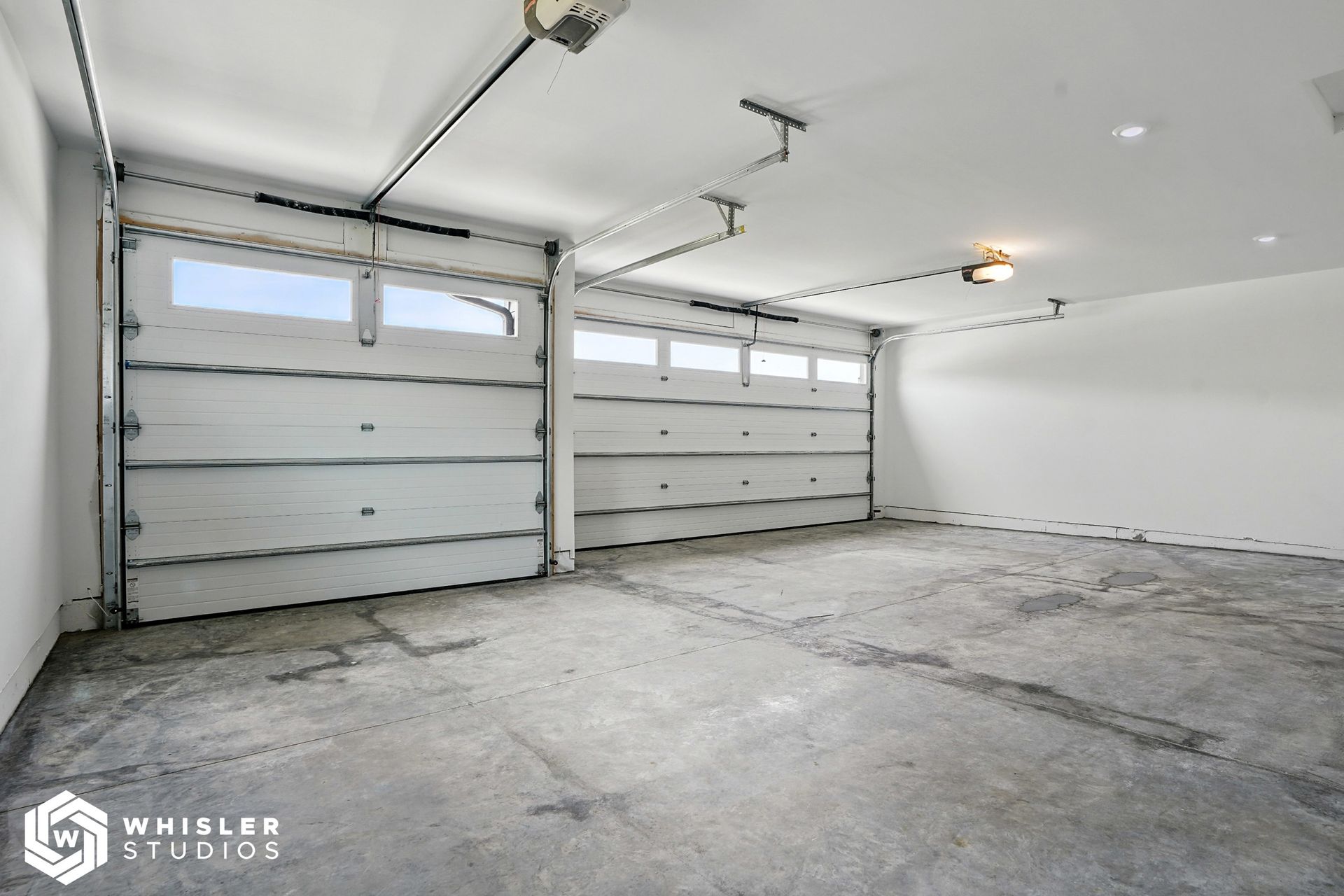 An empty garage with a garage door open and a light on the ceiling.
