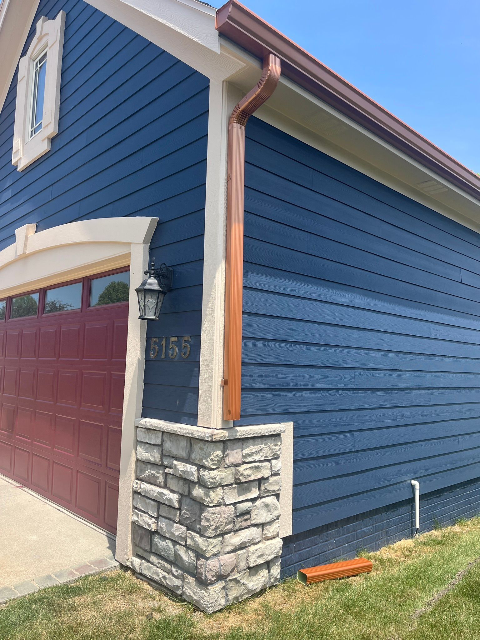 A blue house with a red garage door and a copper gutter