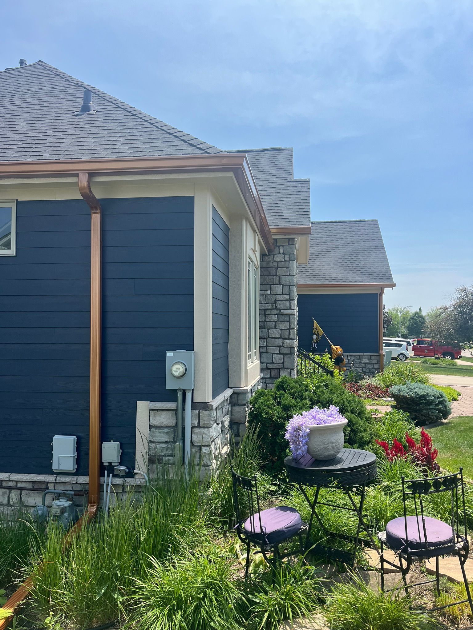 A blue house with a copper gutter and a table and chairs in front of it