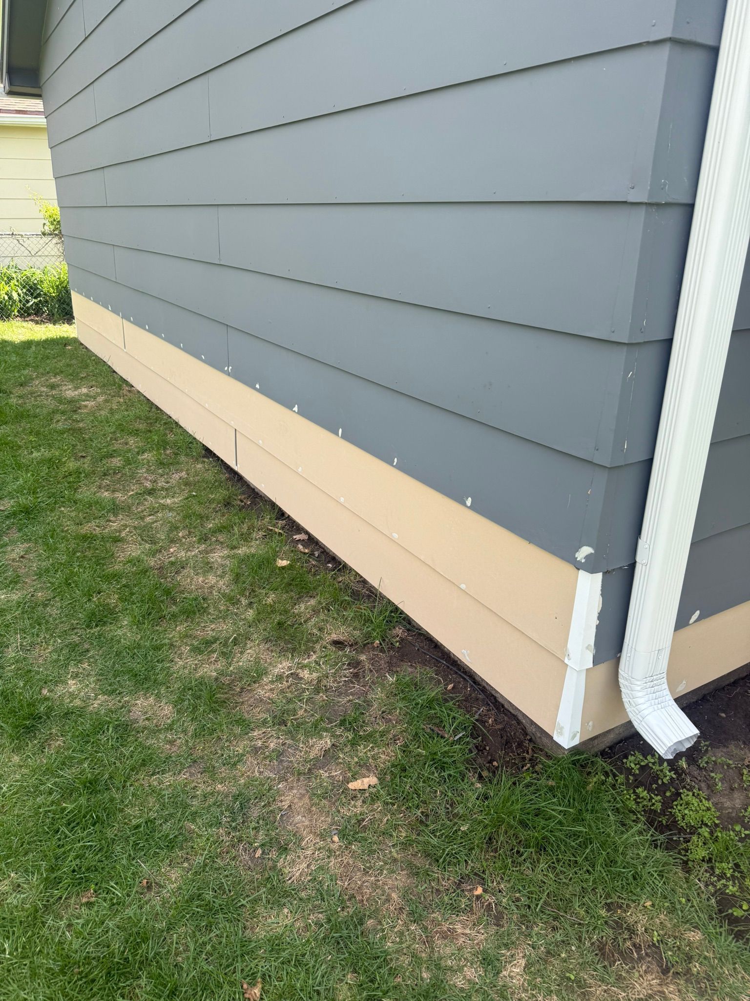 A house with a gray siding and a white gutter is sitting on top of a lush green lawn