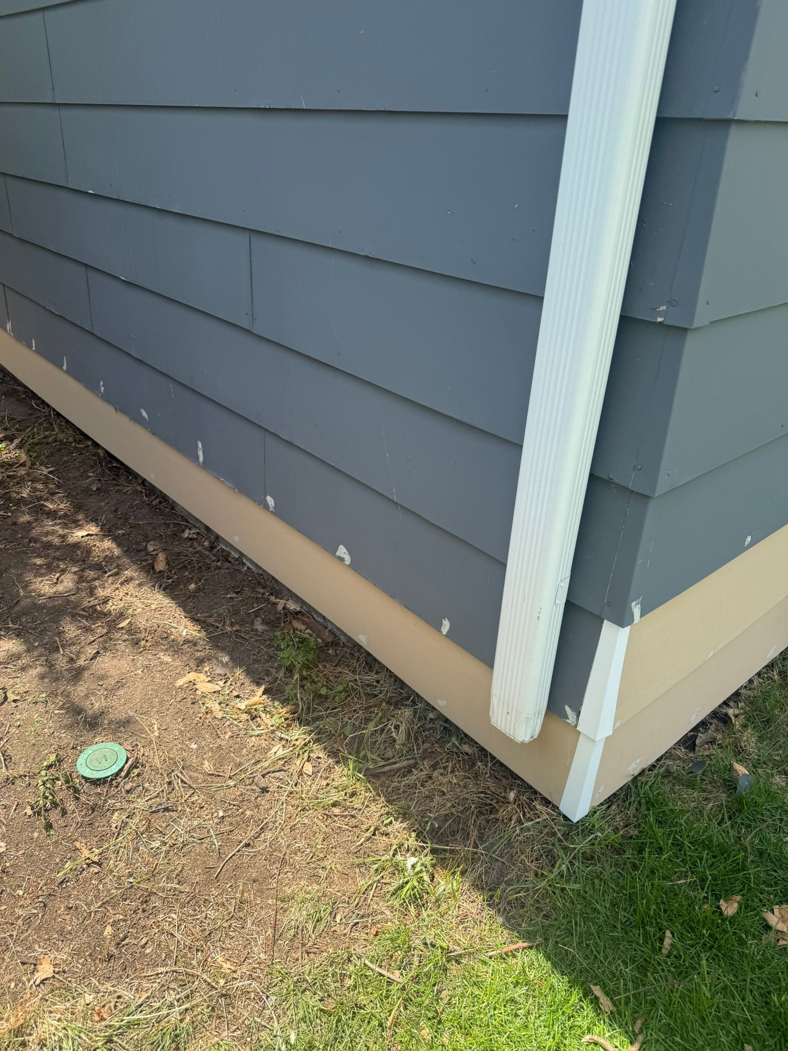 A gray house with a white trim is sitting on top of a lush green field