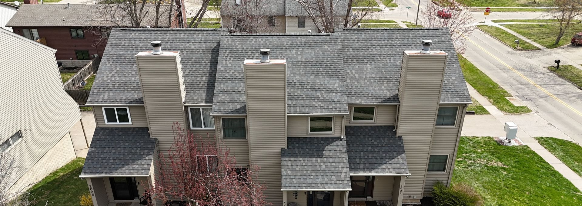 An aerial view of a house with a roof and chimneys in a residential area.