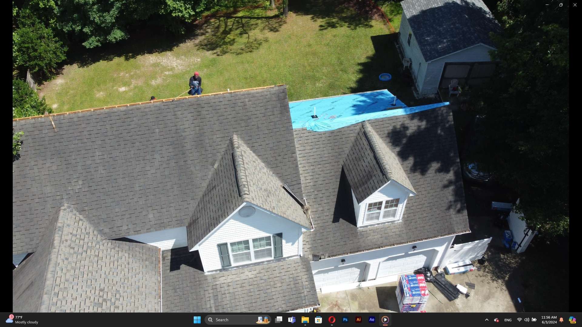 Overhead view of a house with a partially replaced roof and a worker on top.