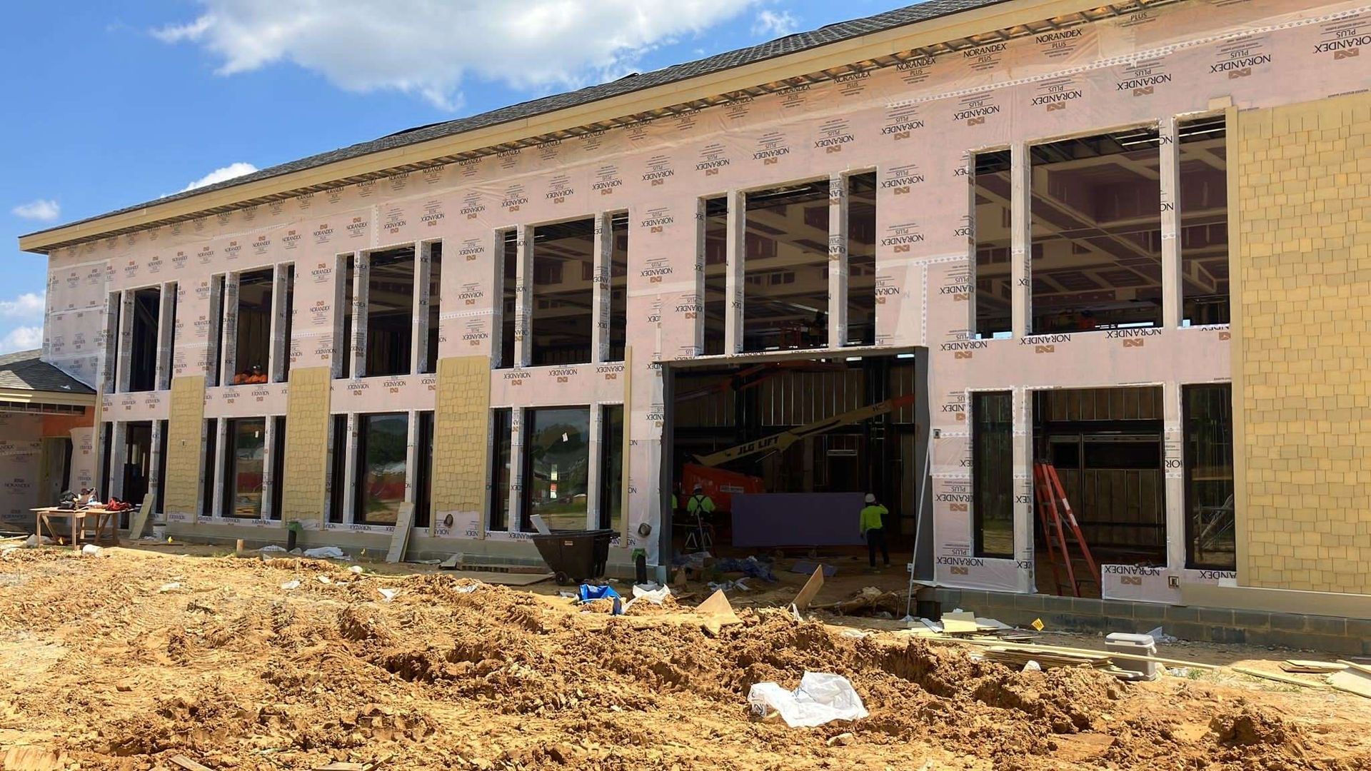 Exterior of a building under construction with multiple windows, pink insulation, and workers. Sunny day.