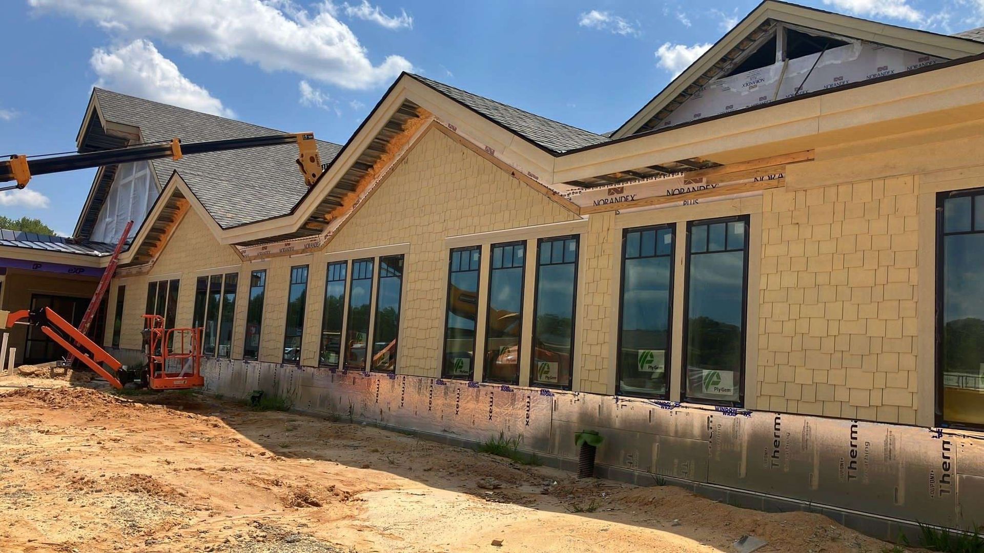 Building under construction, with tan siding, dark window frames, and a crane.