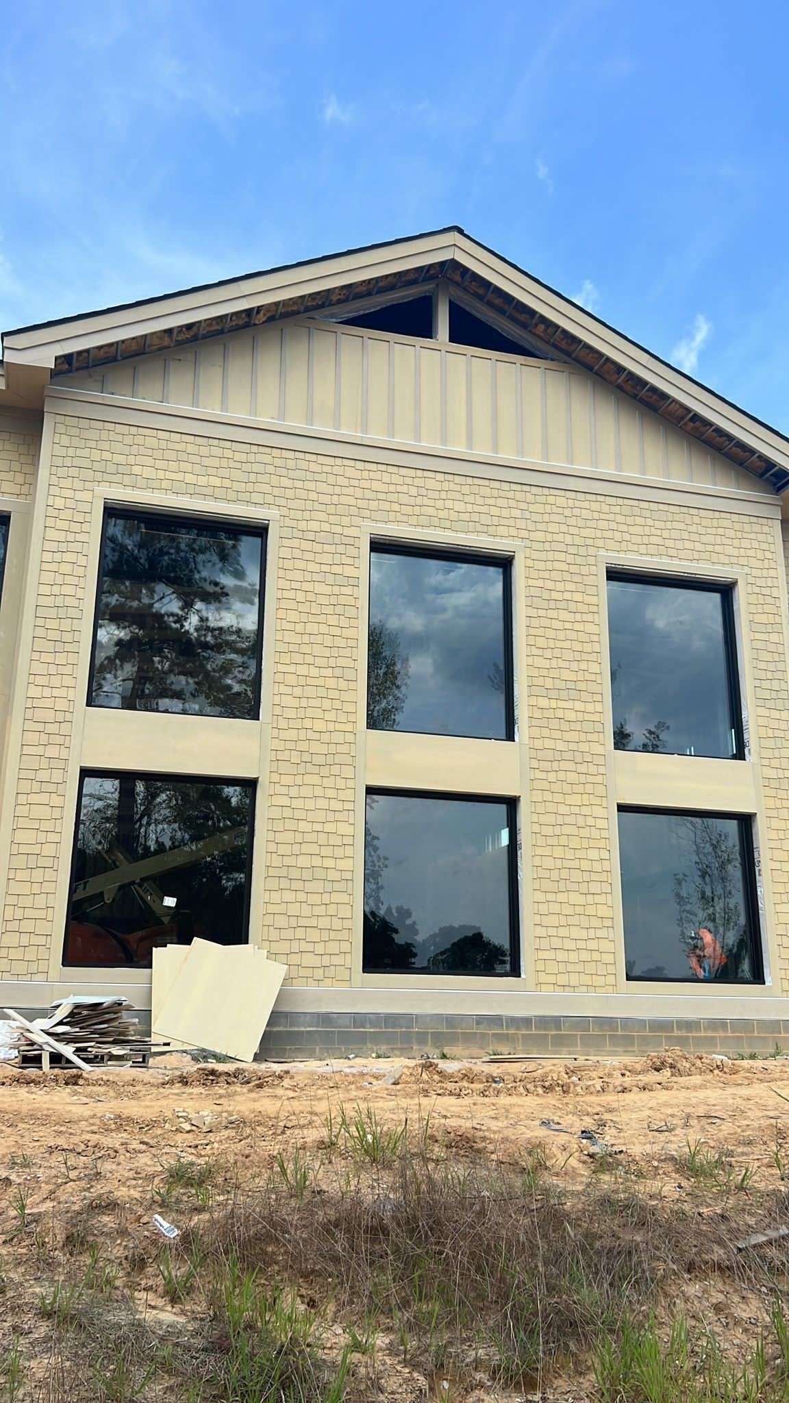 Building exterior with large windows under construction, beige siding and blue sky.