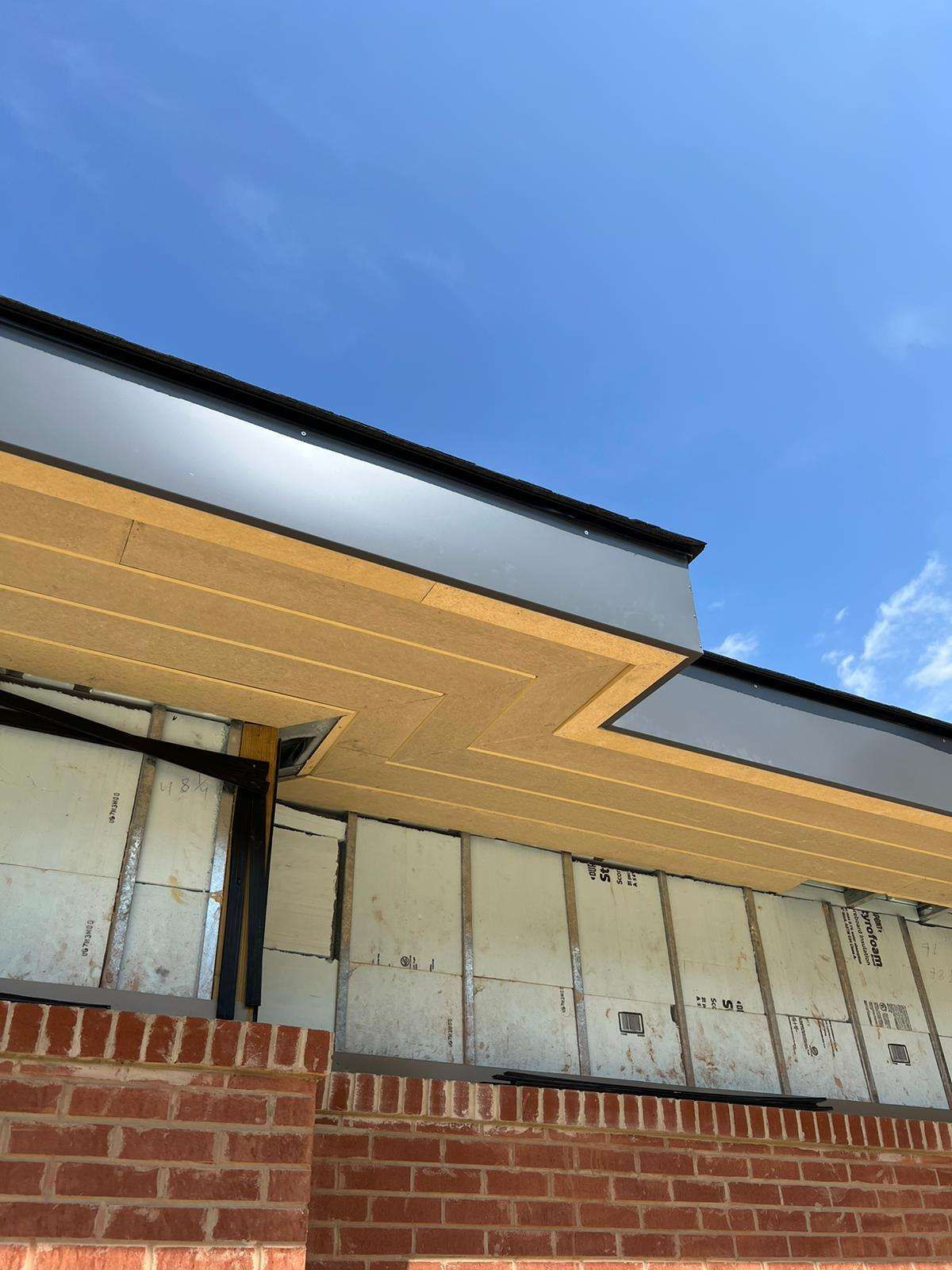 Exterior of a building under construction with brick, insulation, and black overhang against a blue sky.