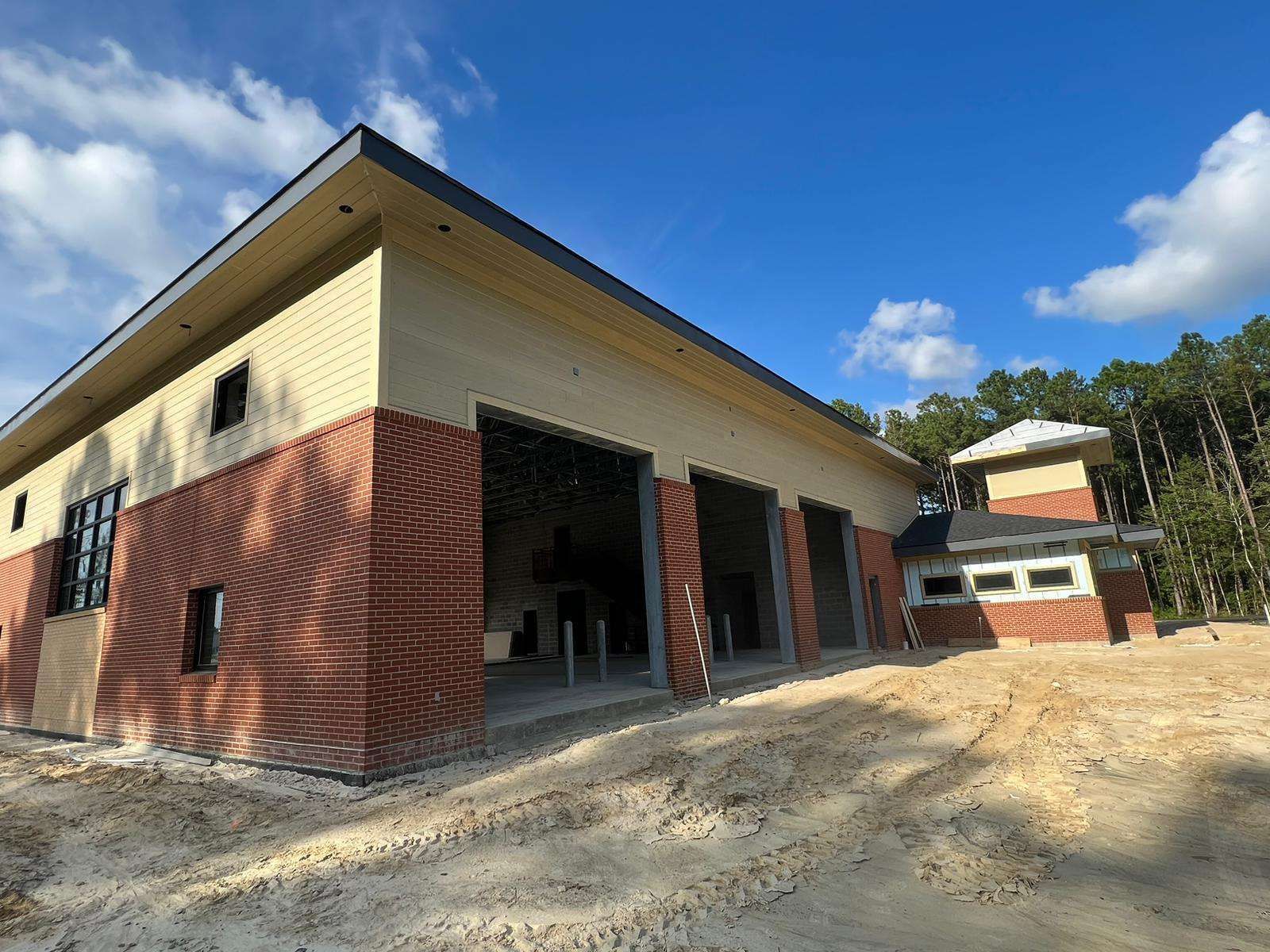 Fire station with tan and red brick exterior; open garage doors, blue sky.