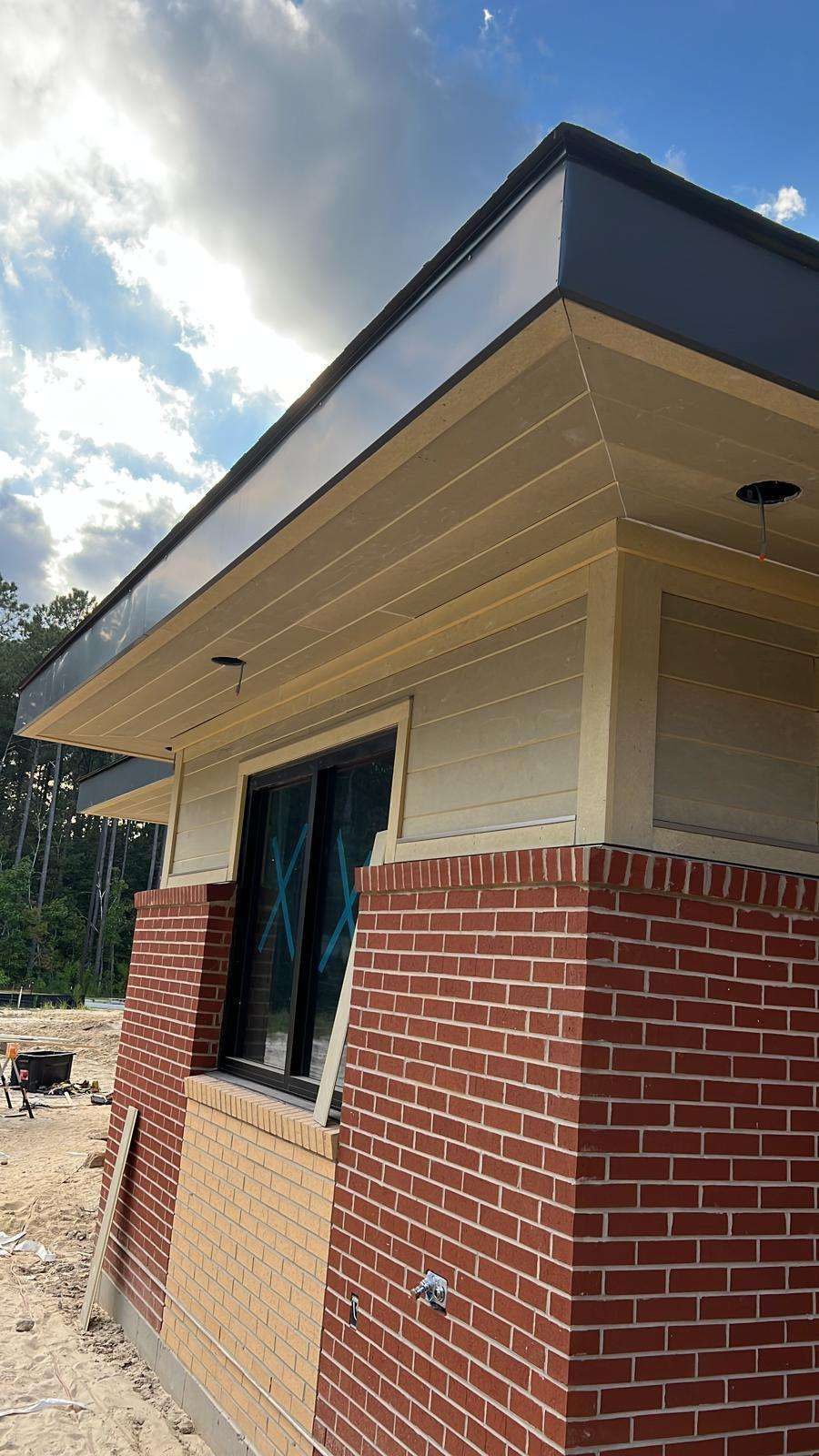 Brick and tan building with dark trim, window, and cloudy sky.