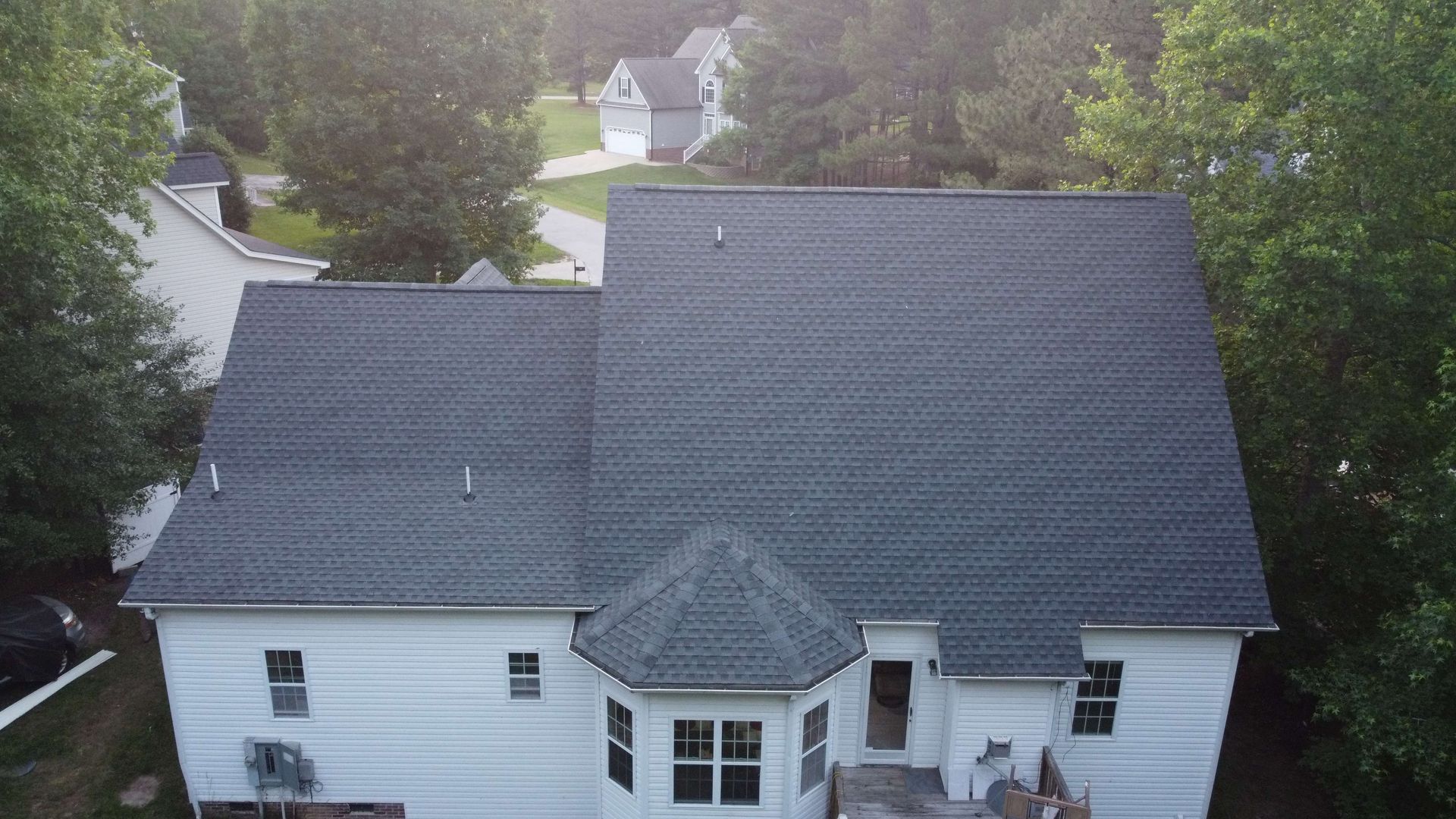Overhead view of a white house with a dark gray roof surrounded by trees in a residential neighborhood.