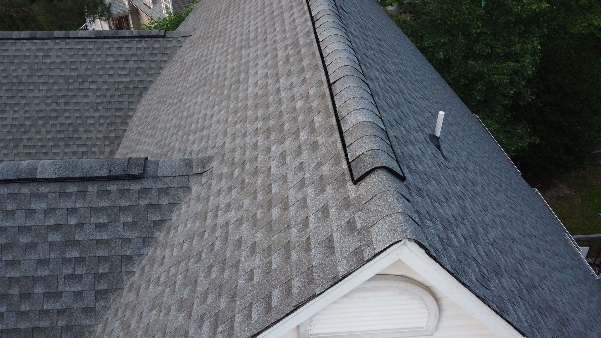 Gray shingled roof corner with a white gable and a pipe.