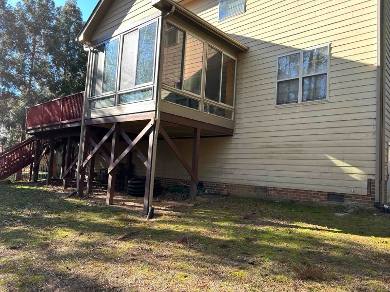 A house with a wooden deck and screened porch. Yellow siding, brown supports, and green grass.