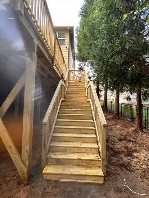 Wooden staircase leads up to a deck. Sunlight on new construction. Outdoors, backyard setting.