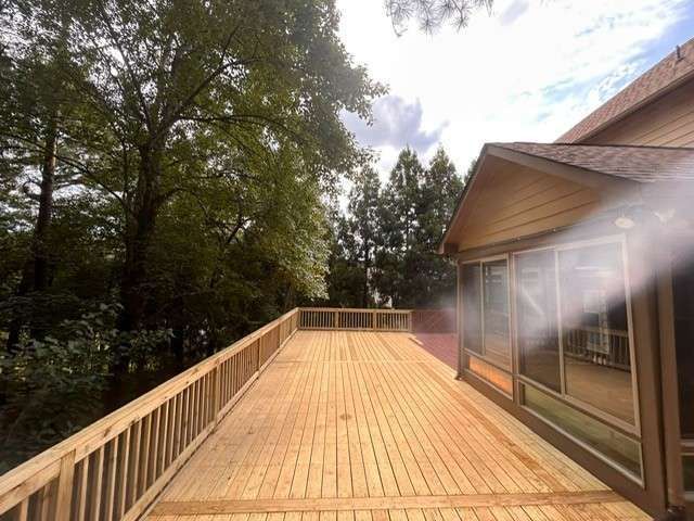 Wooden deck next to a house with a screened-in porch, surrounded by trees. Cloudy sky overhead.