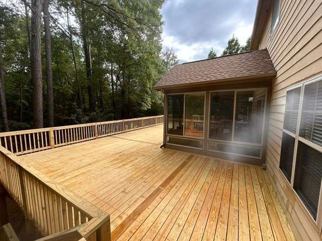 Wooden deck with a screened-in porch attached to a house, surrounded by trees.