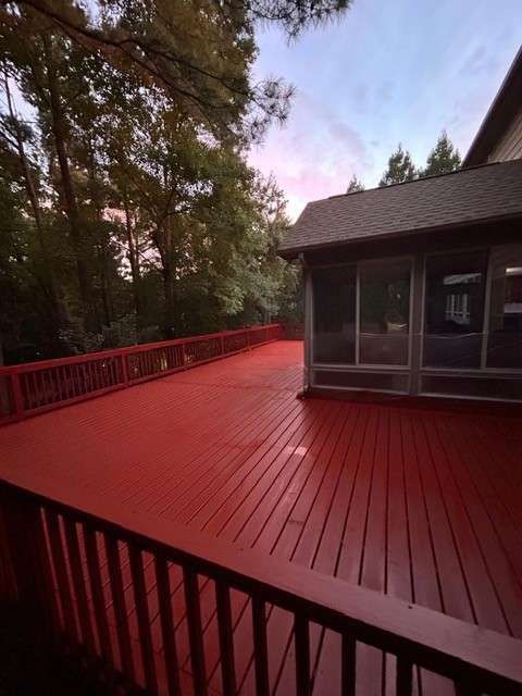 Red-painted wooden deck with railing and a screened porch, surrounded by trees under a twilight sky.