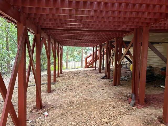 Underneath of a red wooden deck, supported by red wooden posts, with a dirt ground.