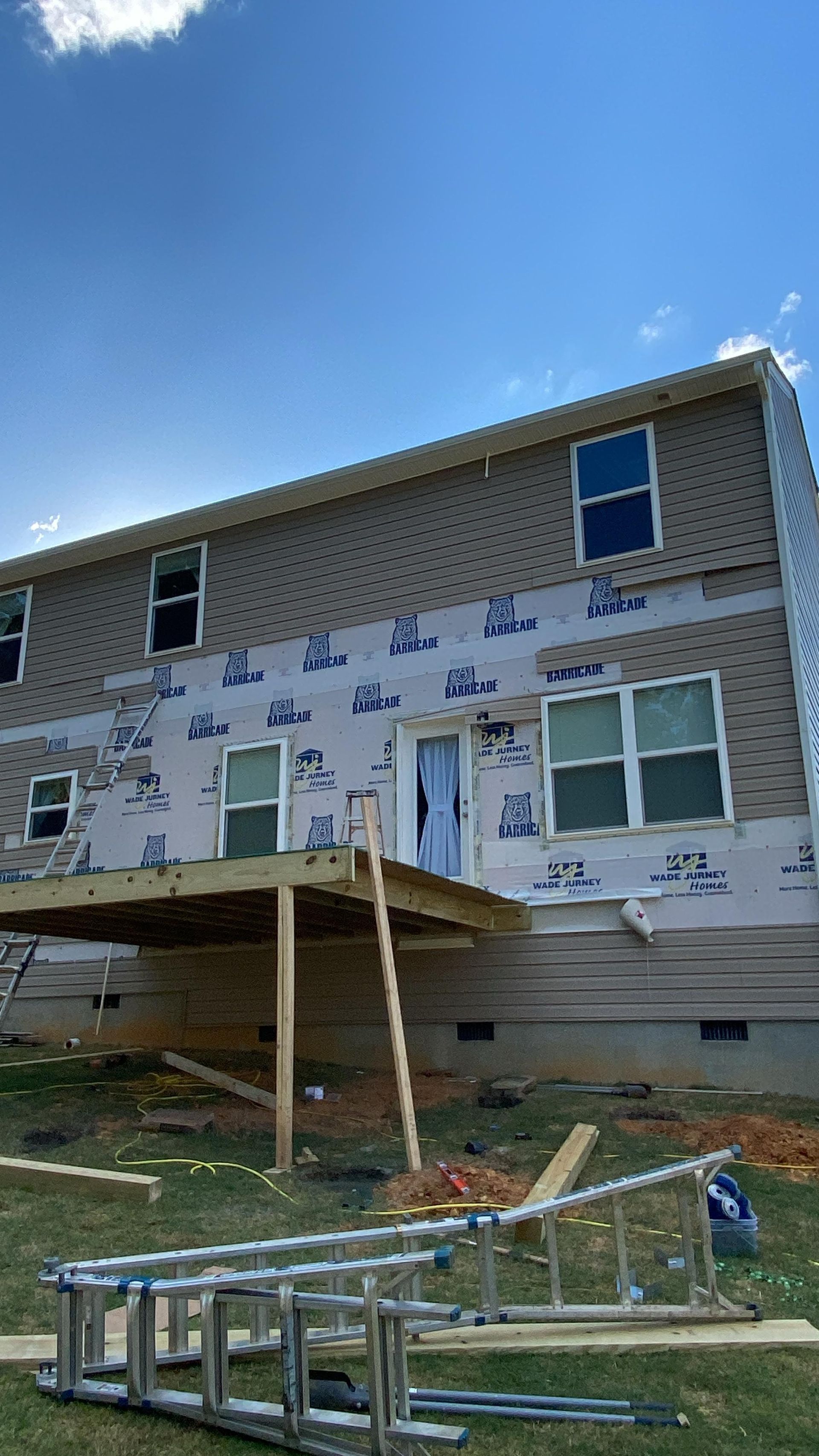 House exterior under construction, with new siding and a deck. Blue tarp covers lower portion.