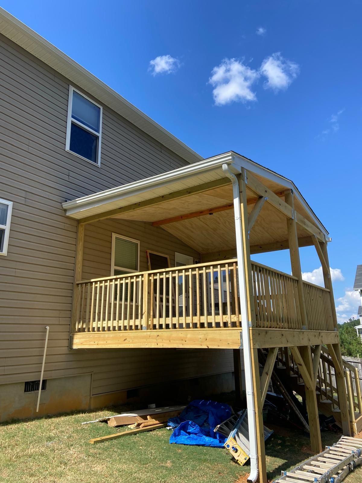 Wooden deck with roof, overlooking a backyard, attached to a beige house on a sunny day.