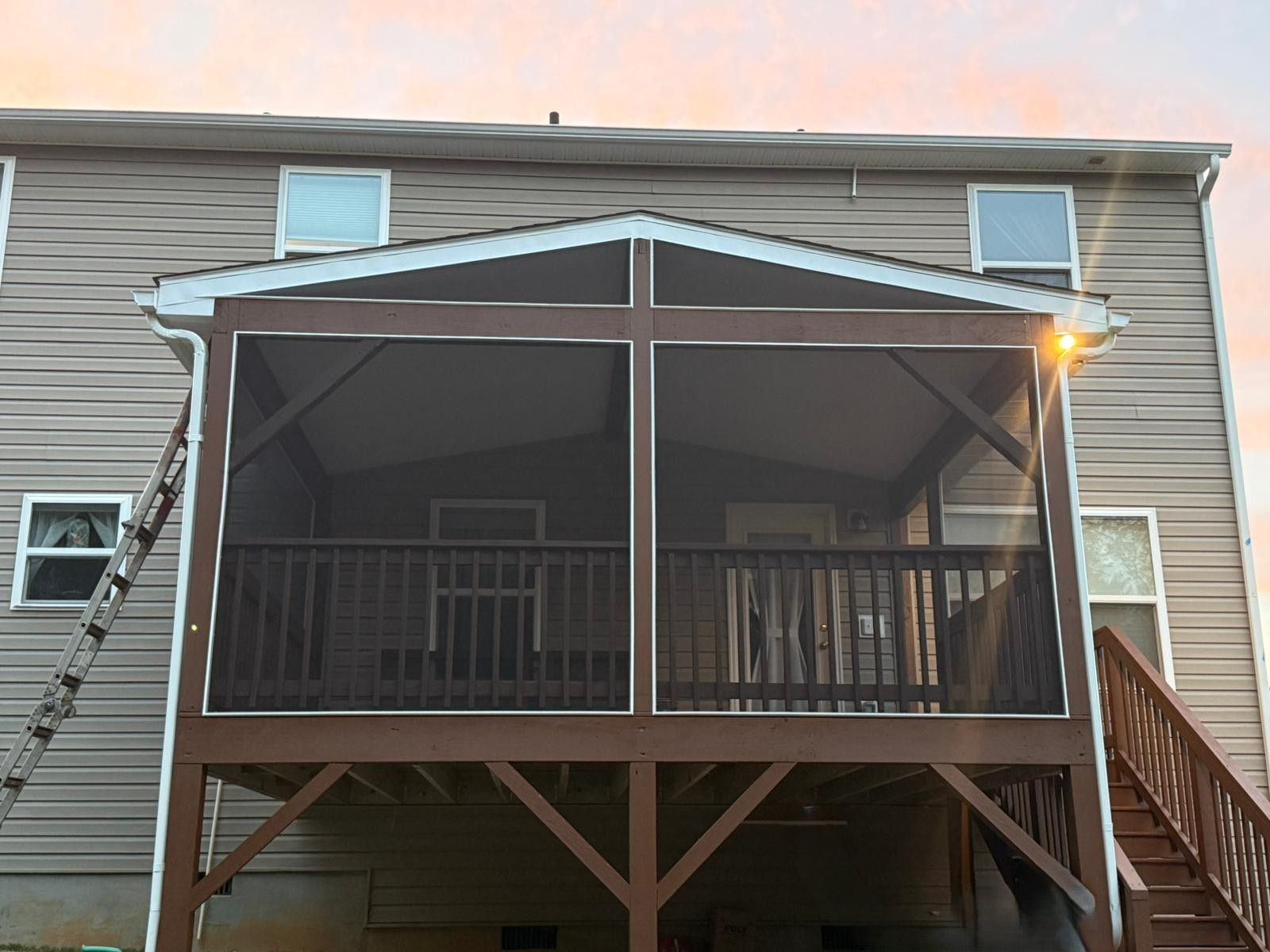 Brown screened-in porch attached to a tan house with windows. A ladder leans against the house.