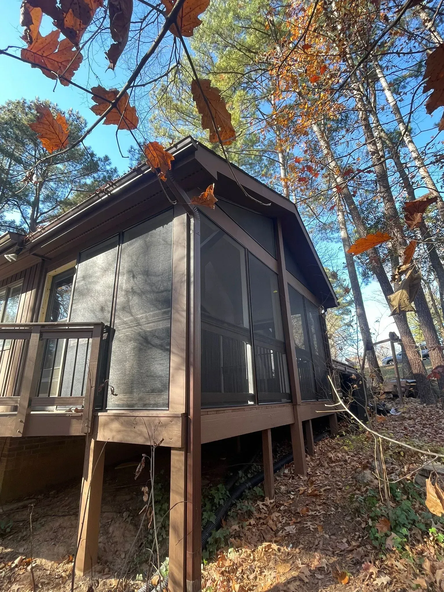 A small house with a screened in porch in the woods.