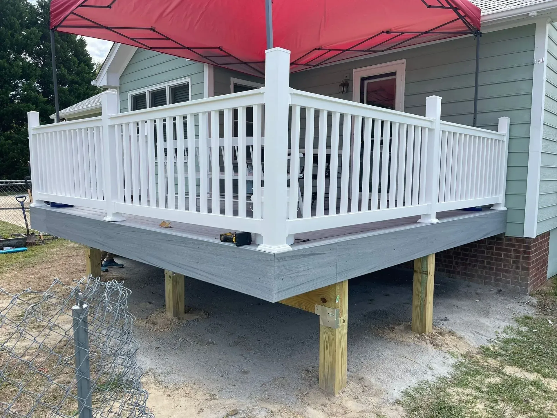 A white deck with a red tent on top of it in front of a house.