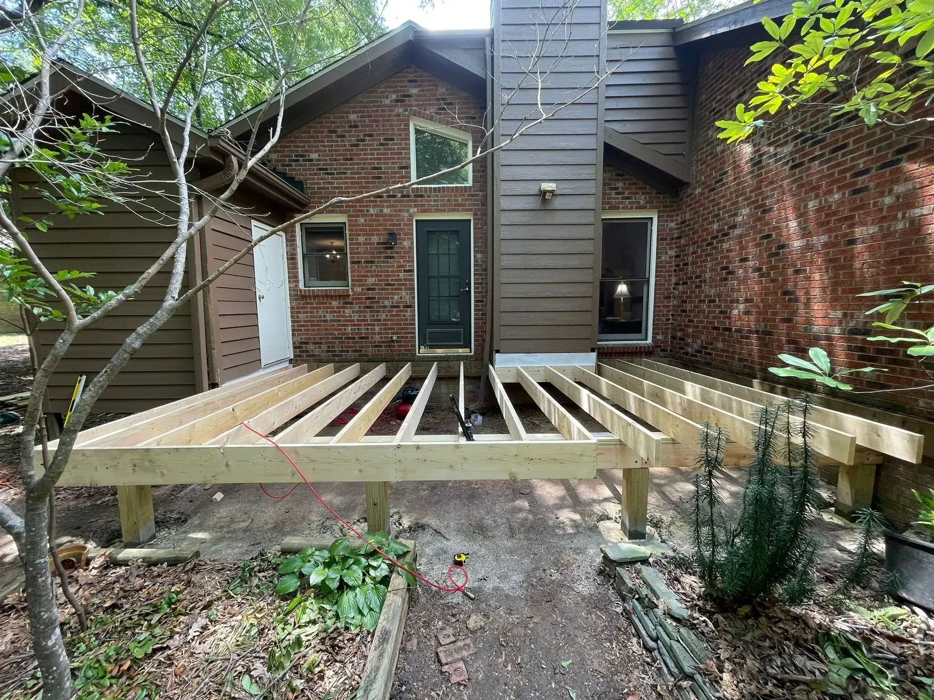 A wooden deck is being built in front of a brick house.