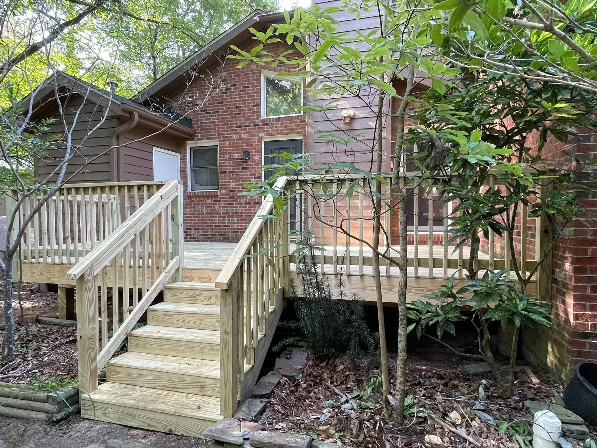 A wooden deck with stairs leading up to it is in front of a brick house.