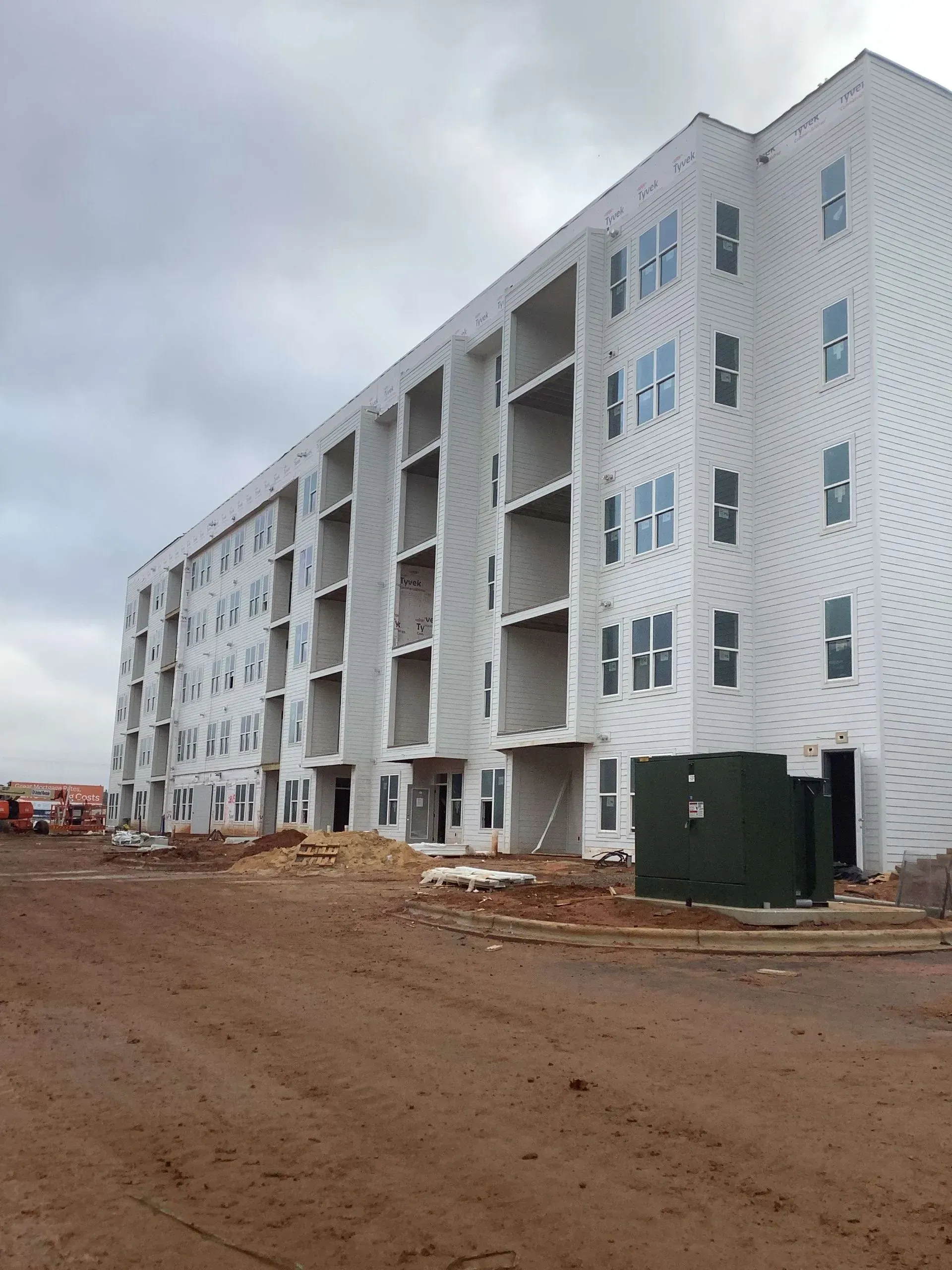 A large white building is being built in a dirt field.